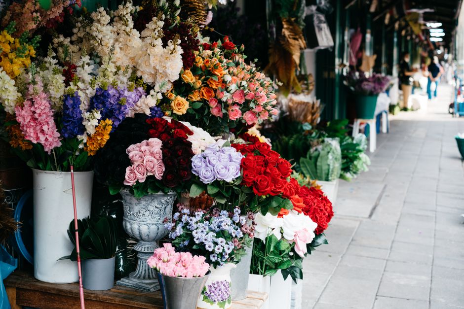A vibrant outdoor display of floral arrangements at a flower shop, featuring a variety of fresh flowers including pink roses, red roses, lavender lisianthus, white orchids, yellow and purple hyacinths